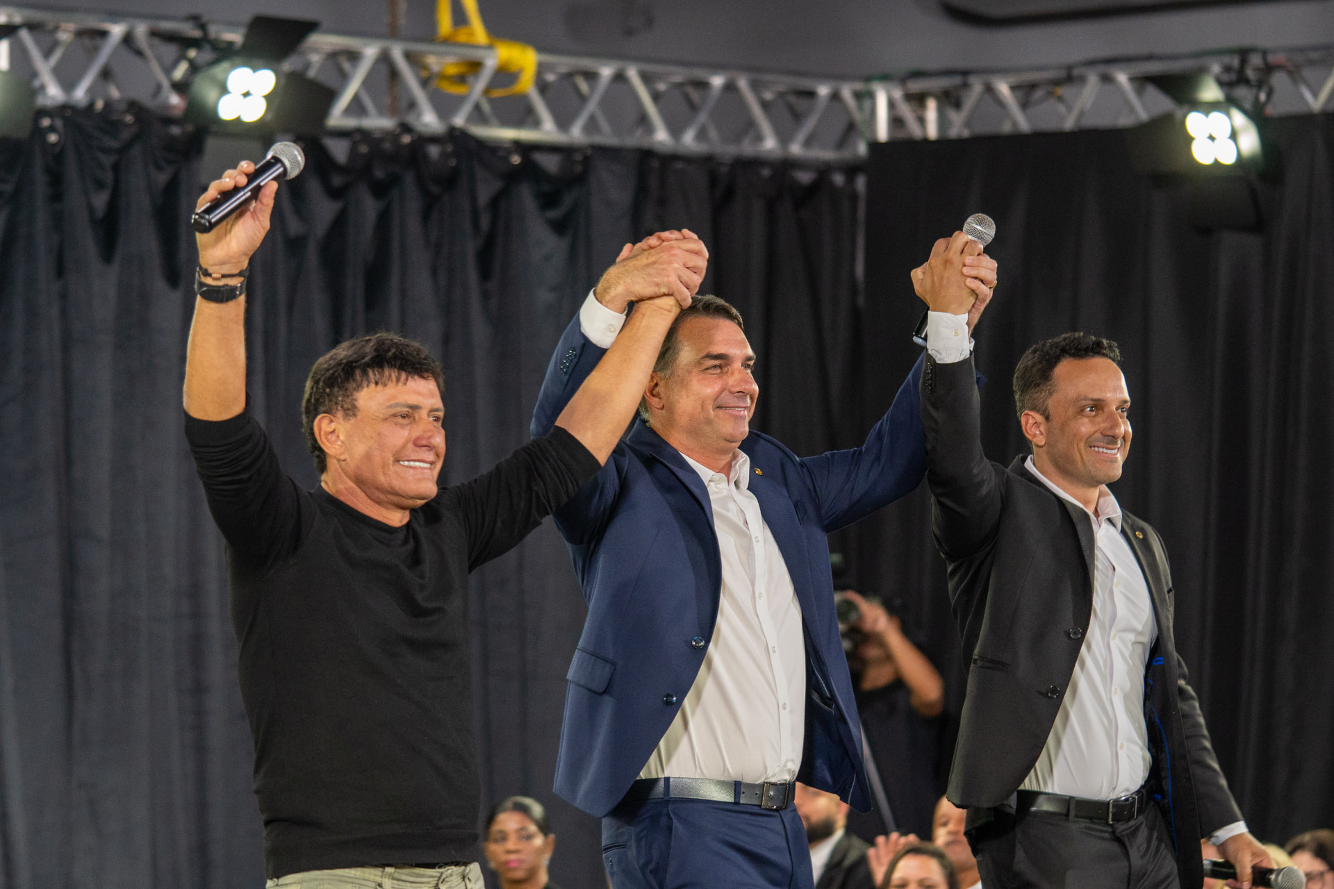 Rogério Barra abraça Del Éder Mauro no palco, ao lado do senador Flávio Bolsonaro